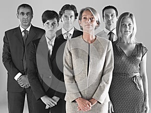 Ambitious businesswoman with team of professionals against gray background photo