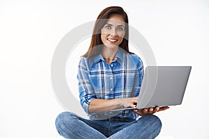 Ambitious cheerful good-looking european woman sit crossed legs in jeans, hold laptop, smiling broadly, working remote