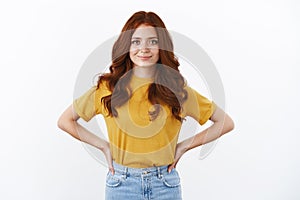 Ambitious and confident cute hipster girl with red curly hair in yellow t-shirt hold hands on waist motivated and self