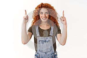 Ambitious redhead female actress dreaming become top, pointing fingers up with confident expression, smiling with white