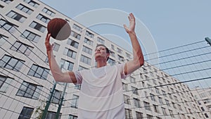 Ambitious strong guy doing exercise with basketball on cityscape background. He shows dribbling streetball tactic