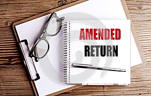 Amended return text on notepad with pen, glasses and clipboard on wooden office desk