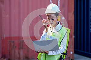 American African factory worker woman talk to red walkie-talkie and laptop for her working in container shipping area. Concept of