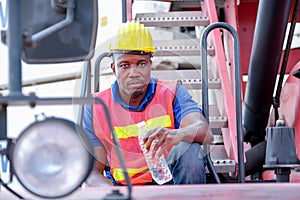 American African technician or factory worker hold bottle of water stay on big crane tractor. Concept of good system and manager
