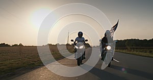 American bikers at sunset. They are driving on the highway with the U.S. flag