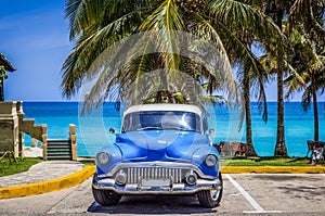 American blue Buick Eight classic car parked under palms on the beach in Varadero Cuba -Serie Cuba