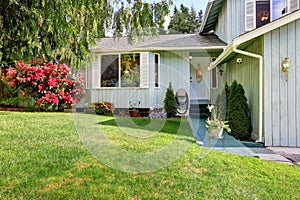 American blue house with white entrance door and green lawn in the front of the house.