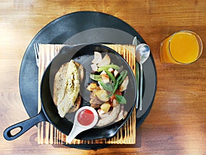 American Breakfast set, Omelette, sausage, bacon, fresh tomato and vegetable in black plate with spoon fork and knife on a wooden