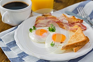 American breakfast with sunny side up eggs, bacon, toast, pancakes, coffee and juice