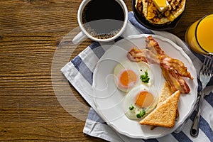 American breakfast with sunny side up eggs, bacon, toast, pancakes, coffee and juice