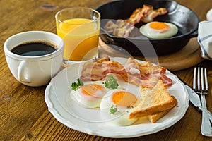 American breakfast with sunny side up eggs, bacon, toast, pancakes, coffee and juice