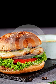 American burger with chicken cutlet, tomato, cucumber, green sauce. Sauce and for french fries on a black stone slate board