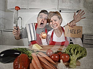 American couple in stress at home kitchen in cooking apron asking for help frustrated