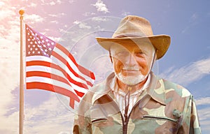 An American cowboy is standing against a blue sky with a developing American flag. He is wearing a straw cowboy hat. Elements of