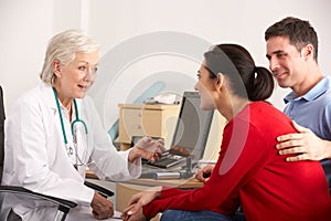 American doctor talking to happy couple in surgery