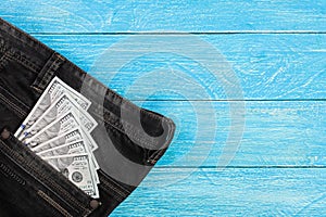 American dollar bills in jeans pocket on blue wooden background with copy space for your text. Top view