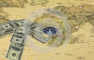 American dollars in form of arrow that indicates direction and navigation compass on old vintage world map as symbol of tourism wi