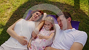 American dream family relax on the lawn in the shade, lie on a purple blanket, carpet or rug. Father, mother and