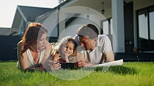 American dream family relax outdoors near the house on the lawn, lie on a purple blanket, carpet or rug. Father, mother