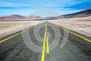 American empty desert asphalt road from low angle with mountains and clouds on background. South american highway in Atacama deser