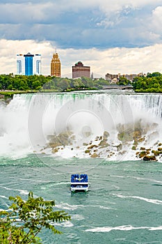 American Falls, a boat in the mist, and buildings of american Niagara Falls city, viewed from Niagara Falls, Ontario