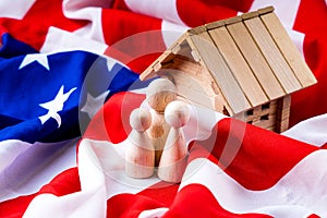 American family concept with wooden figurines of people and toy wooden house standing on the flag of America