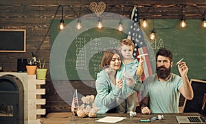 American family at desk with son making paper planes. Homeschooling concept. Kid with parents in classroom with usa flag