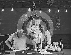 American family at desk with son making paper planes. Kid with parents in classroom with usa flag, chalkboard on