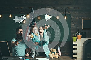 American family at desk with son play with paper planes. Homeschooling concept. Kid with parents in classroom with usa