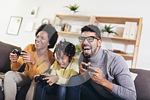 American family at home sitting in sofa couch and playing console video games together