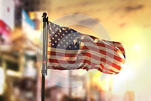 American Flag Against City Blurred Background At Sunrise Backlight