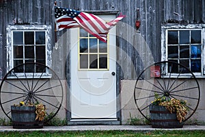 American Flag blowing in the wind by a door and two wagon wheels