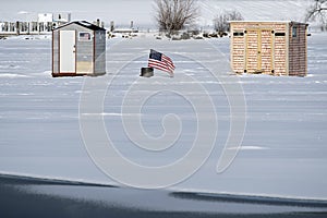 American Flag Displays Between Two Ice Fishing Shacks Near Lake Shoreline