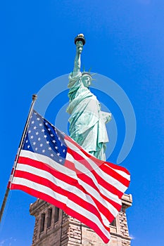 American flag on flagpole waving in the wind against a blue sky with Statue of Liberty