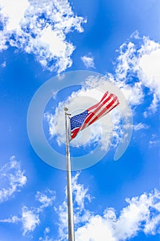 American flag flutters in the wind against the blue sky with white clouds