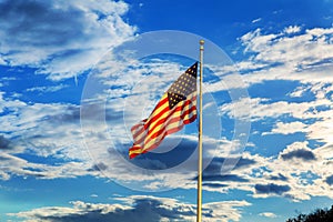 American flag flying in the breeze against blue sky with white clouds