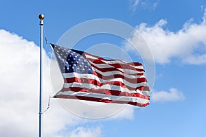 American flag flying in a breeze against a sunny blue sky with light white clouds