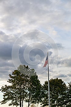 American flag flying on a cloudy day with trees in the background