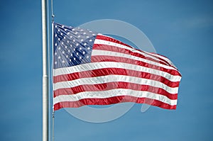 American flag flying at half mast against blue sky