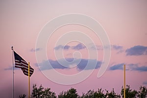 American flag flying near football goal posts during sunset with cumulus clouds along treeline