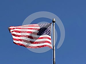 American flag on a metal flag pole waving high on the air in blue sky in bright sunlight