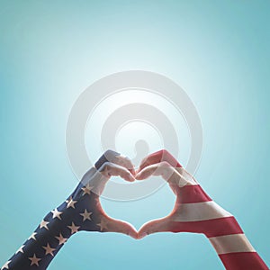 American flag pattern on people hands in heart shaped form against vintage sky background w clouds