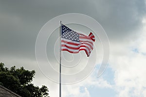 American flag, Stars and Stripes, flying from a flagpole against dark, stormy clouds in the background.