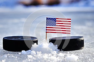 Americká vlajka na párátko mezi dvěma hokejovými puky. Spojené státy budou hrát na mistrovství světa ve skupině A. 2019 IIHF World