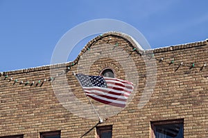 American flag waves from retro southwestern style brick building facade hung with party lights