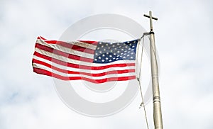 American flag waving in the wind on a flagpole with  christian cross on top. Patriotism and religion concept