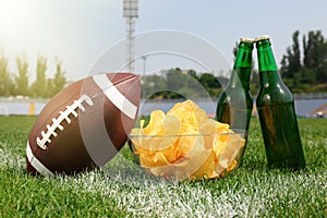 American football ball with beer and chips on green field grass in stadium