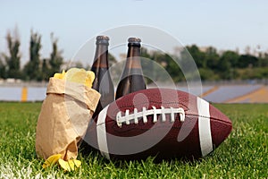 American football ball with beer and chips on green field grass in stadium