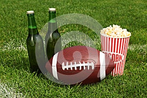 American football ball with beer and popcorn on green field grass