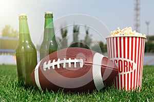 American football ball with beer and popcorn on green field grass in stadium